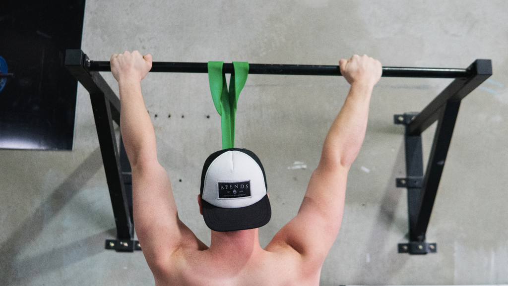 man doing assisted pull-ups in gym using green resistance band