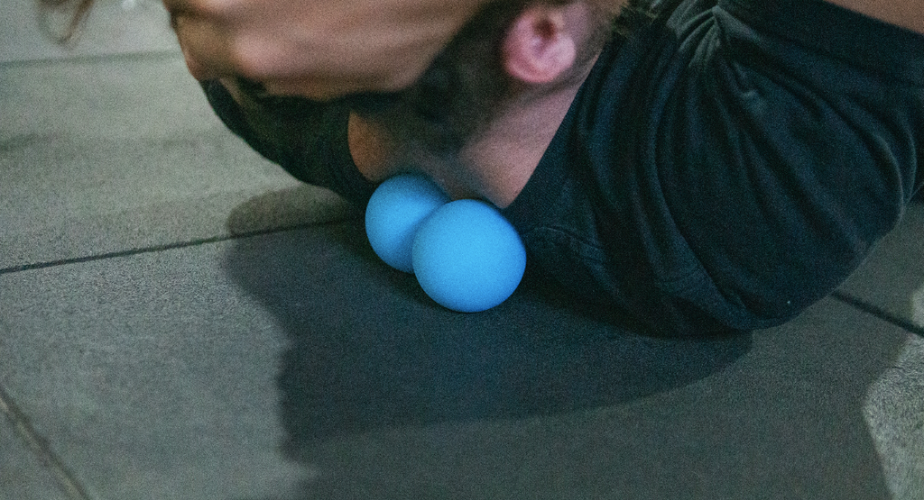 man lying on ground releasing tight muscles with a blue peanut trigger ball