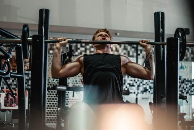 man wearing black tank top in gym holding barbell