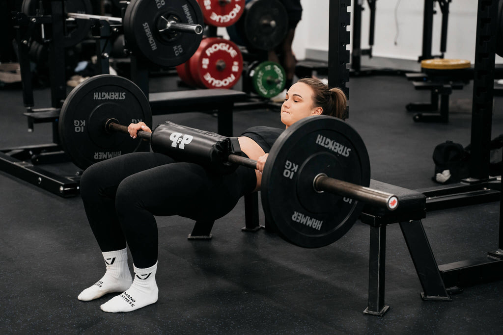 girl using barbell hip thrust pad in gym while hip thrusting